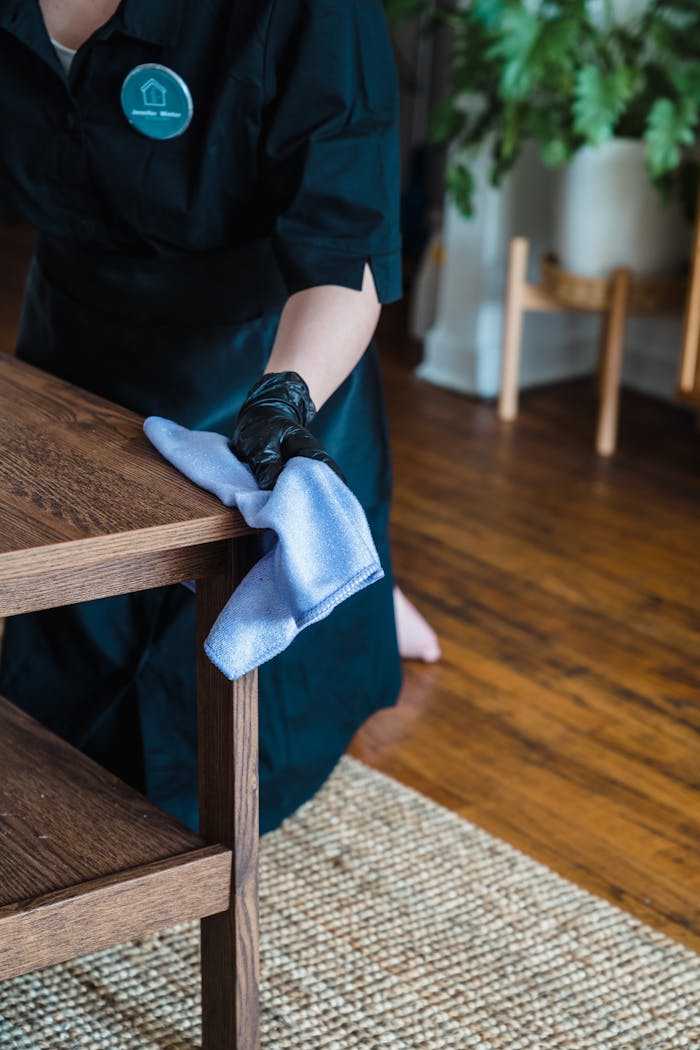services-04 Person in uniform cleaning a wooden table indoors with a cloth.